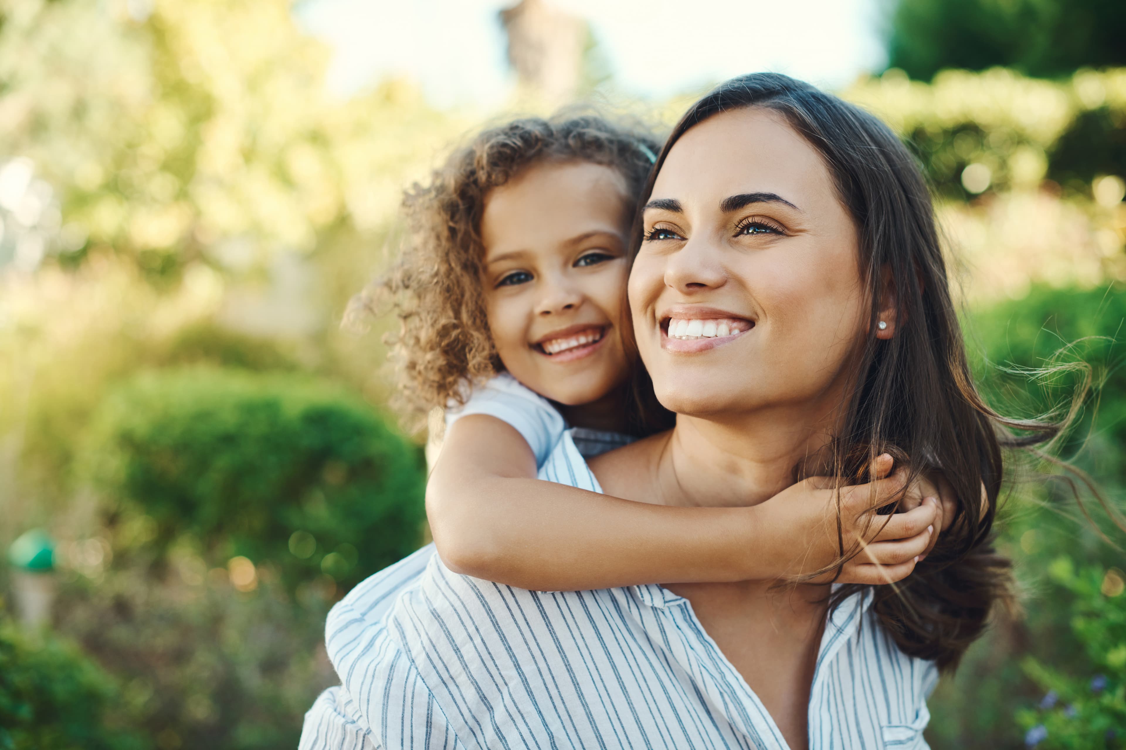 Mother carrying her smiling daughter on her back outdoors